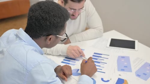 Two People Analyzing Charts at White Table