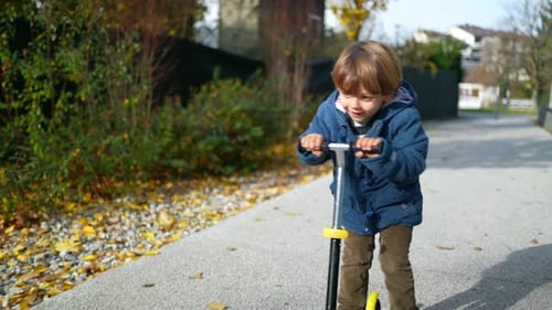 Joyful Three-Year-Old Boy Riding Toy Scooter Outdoors in Autumn Sunshine