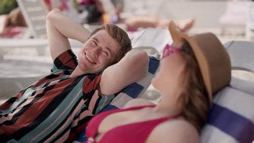 Young Couple Relaxing at a Tropical Beach Resort Sunbathing and Smiling Under the Sunlight