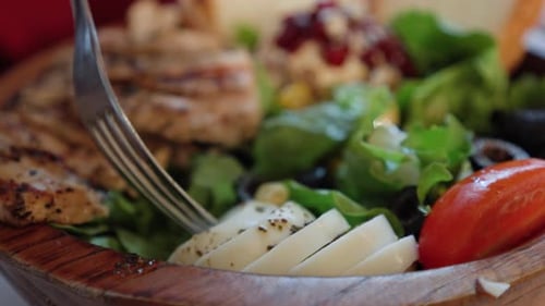 Person, die gekochte Eierscheiben auf gegrilltem Hähnchen und Gemüsesalat auf einer Holzschale mit einem Deckel isst