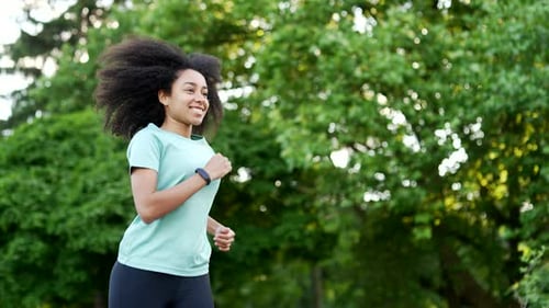 Young african american female runner jogging in an urban city park. Happy sportswoman enjoys jogging