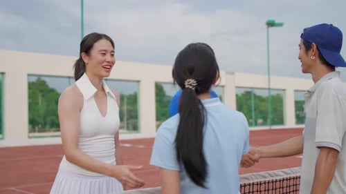 Group of Asian friends playing tennis match on an outdoor clay court.