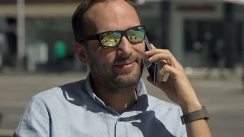 Young Man Drinking Coffee and Talking on Cellphone in Cafe in City 30s