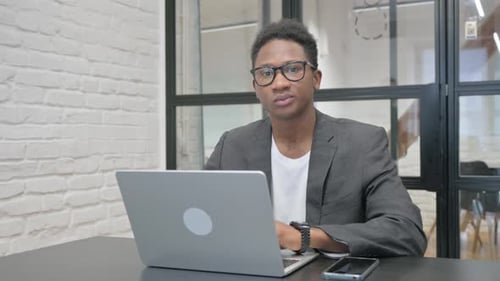 Young African Man Looking at Camera while Working on Laptop in Office