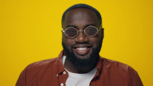 Bearded man smiling with glasses against yellow background