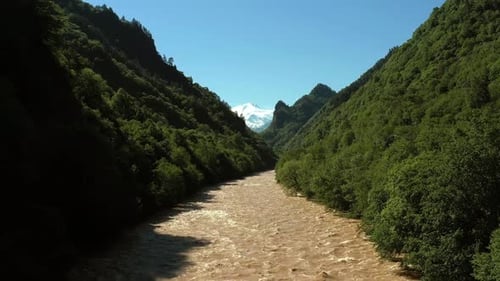 Luftaufnahme eines Flusses, der durch ein üppiges grünes, waldbedecktes Hanggebiet mit Schneedecke fließt