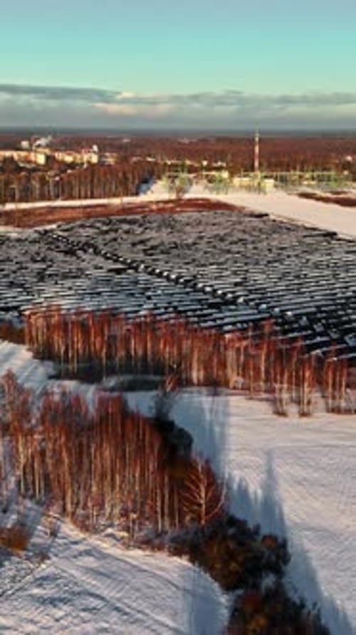 Vertical Aerial of Snow-Covered Solar Farm Panels in Winter by Industrial Factory