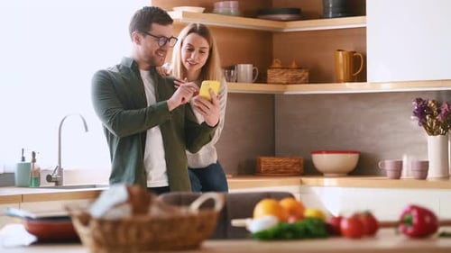 Smiling Couple Using a Smartphone in Modern Kitchen