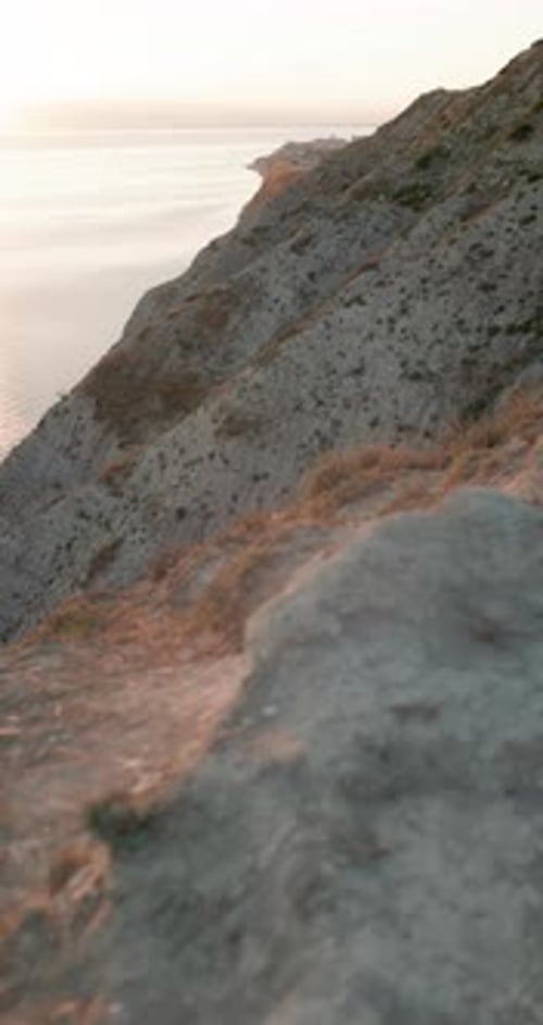 Walking on Rocky Cliff Coastline with Sunset Warm Tones Vertical Footage