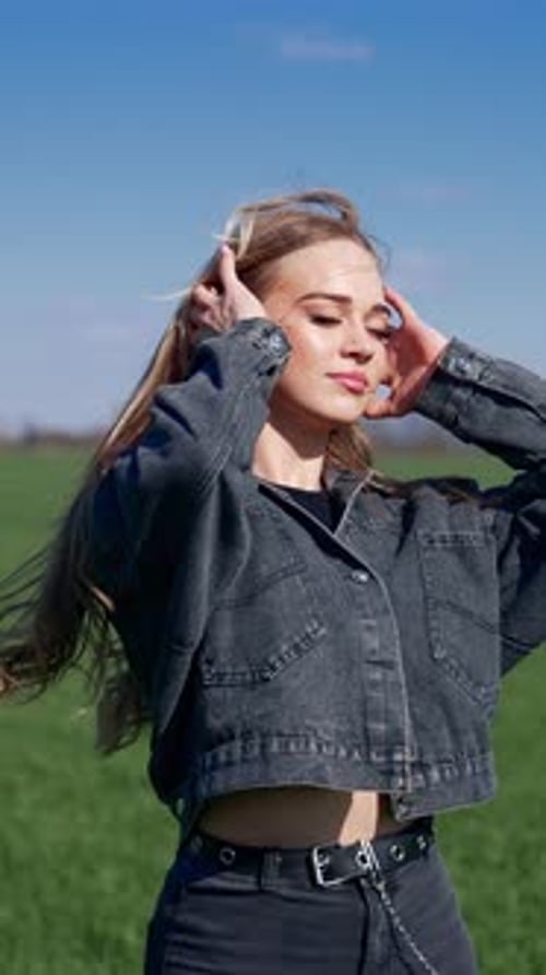 Beautiful girl on field at sunlight. Young woman in denim suit standing with closed eyes to the sun.
