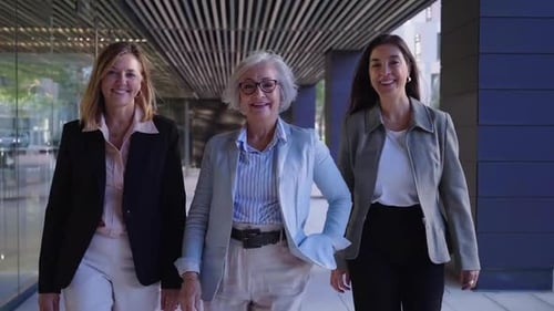 Three Empowered Mature Businesswomen Walk Purposefully Into the Office Looking Cheerfully at the