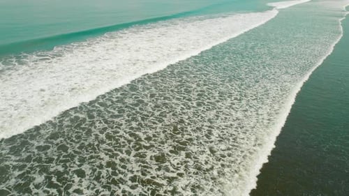 Aerial view of wide rolling ocean waves meeting sandy shoreline on sunny day