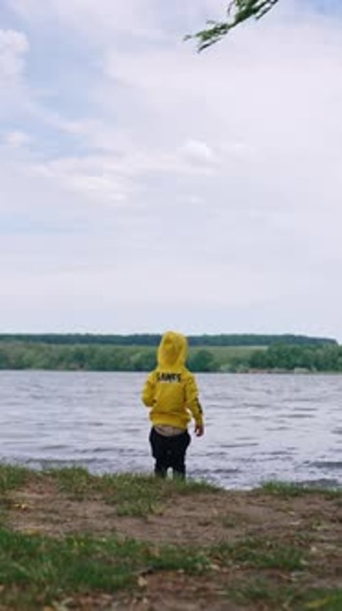 Garoto vestindo um moletom amarelo e calça preta está no lago.