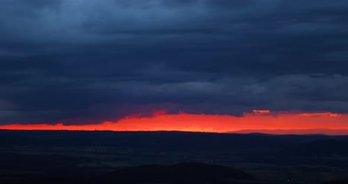 Dark red clouds during sunset open in the gap between the clouds and the horizon.