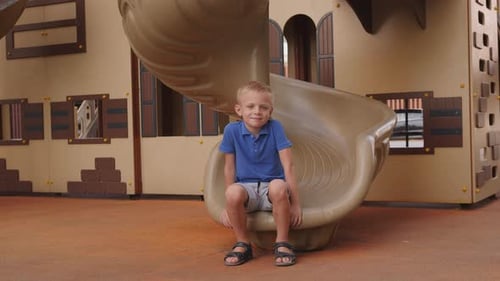 A Small Boy is Sitting on a Slide on the Playground in the Courtyard