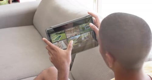 Biracial man using tablet with home security camera views on screen, slow motion