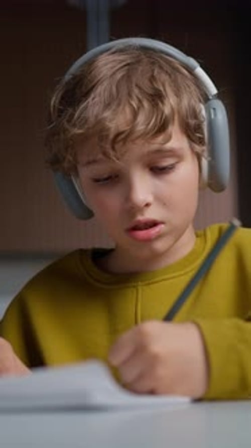 Young Boy Wearing Large Headphones Seated Indoors with a Focused Expression Interacting with a Book