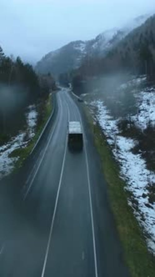 Truck Travels Along a Winding Road Through a Foggy and Snowy Mountain Landscape