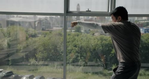 Side View of Asian MMA Fighter Training in Gym Throwing Punches Exercising Against Window Background
