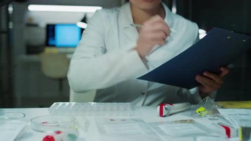 Female Forensic Technician Examining Evidence and Writing Down Notes in Lab