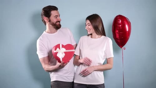 Man Giving Heart-Shaped Gift to Smiling Woman Against Blue Background