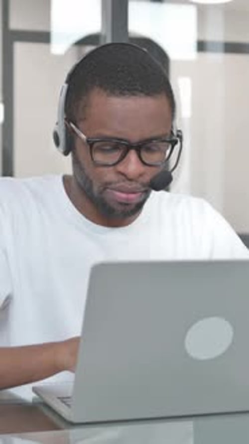 Young African Man with Headset in Call Center Working on Laptop, vertical video