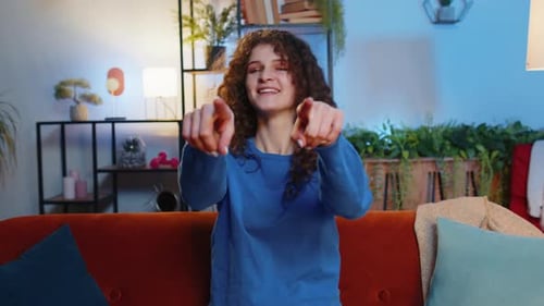 Glückliche Frau, die auf dem Sofa sitzt und mit beiden Händen zeigt, macht das Auswählen und Aussuchen der Geste