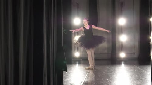 Teenage ballerina practices ballet on stage under bright lights