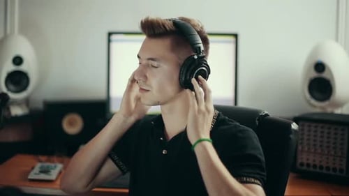 Young sound engineer listening to the music in headphones and turning face back to the camera