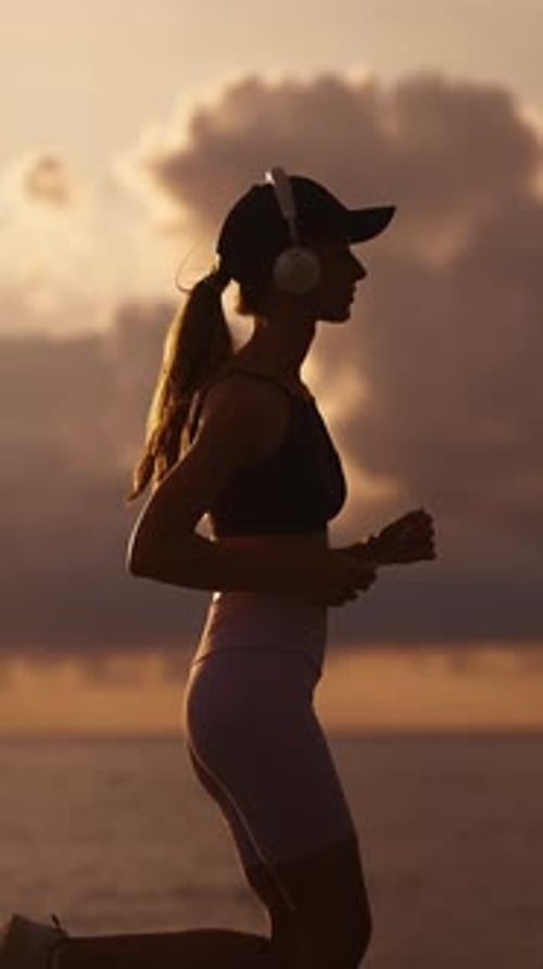 A Young Sporty Woman Runner is Listening to Music in Earphones and Training Slim Fitness Girl is