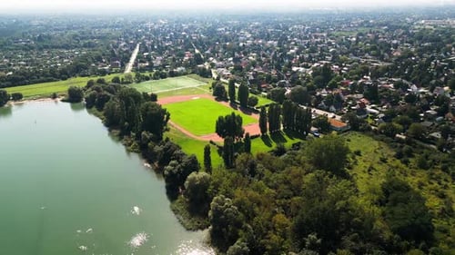 Explorez un paysage estival ensoleillé en Drone : un vaste champ, un lac serein, des baigneurs, une activité