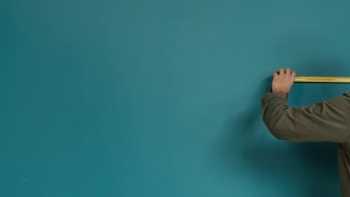 Young Man Measuring Width of Teal-Coloured Wall Using Yellow Flexible Ruler