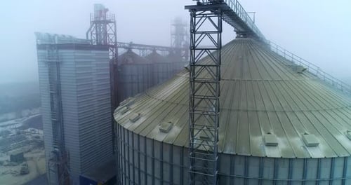 Metal tanks and constructions at modern grain processing plant. Foggy winter weather backdrop.