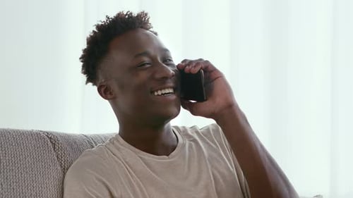Smiling Man Talking on Phone While Sitting on Sofa