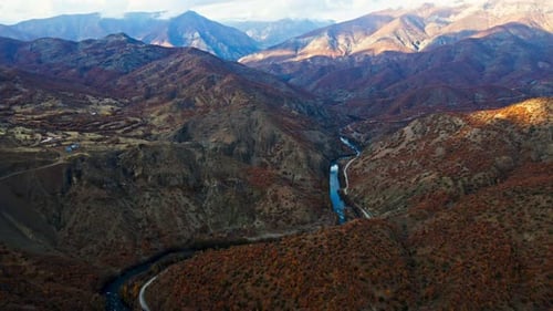 Eine kurvenreiche Straße führt durch ein Tal, an dem ein Fluss vorbeifließt.