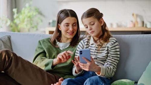 Woman and Girl Using Smartphone Together on Sofa