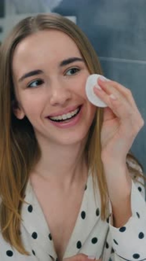 Young Woman Cleans Face in Bathroom Mirror
