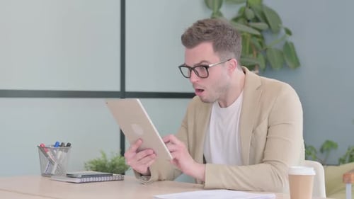 Man Reacting to Tablet Screen at Desk