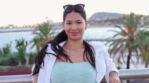 pretty asian woman in summer next to a palm tree on the beach at sunset