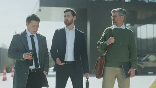 Three Men Dressed in Business Clothing Engage in Conversation During Their Walk Outside Modern