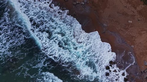 Waves crash on the shore at a rocky beach during daylight hours
