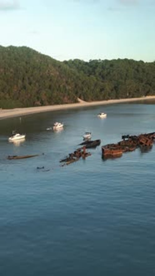 Vertical drone wrapping rusty Tangalooma Wrecks turquoise ocean yachts Moreton Island greenery