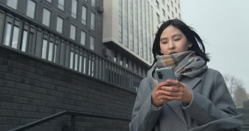 Closeup of a Girl Going Down the Stairs with a Smartphone on the Background of the City