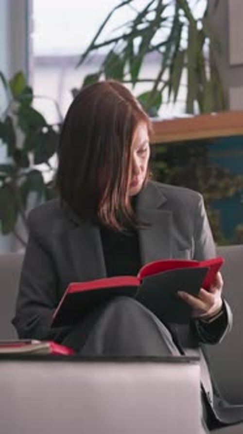 Businesswoman Focused on Reading Red Notebook in Modern Office