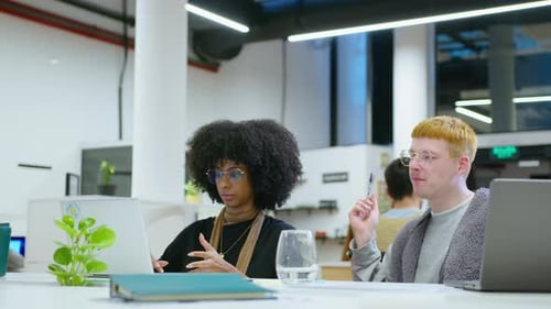 Gen Z Coworkers Using Laptop and Speaking at Workplace in the Office