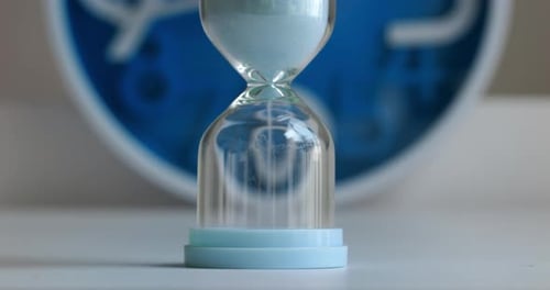 Hourglass Sand Flowing with Clock in Background