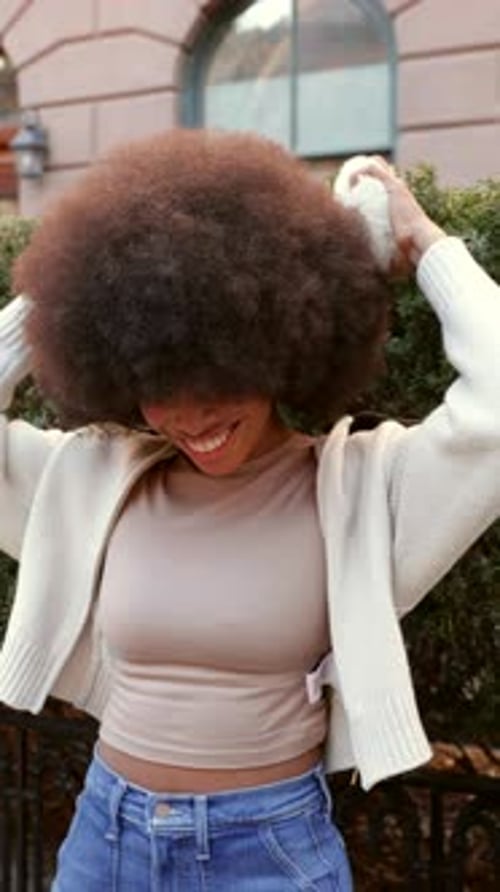 Happy Young Woman with Afro Hairstyle Putting on Earmuffs