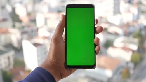 Young Man Hand Using Smart Phone with Green Screen Against City Buildings