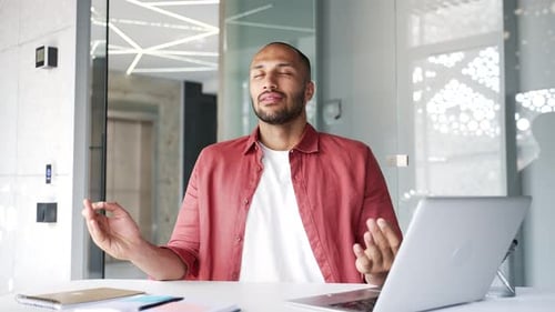 Businessman meditating with closed eyes during a break while sitting at workplace in business office