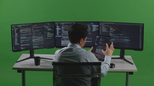 Asian Man Working With Tablet While Write Code With Multiple Computer Screens In Green Screen